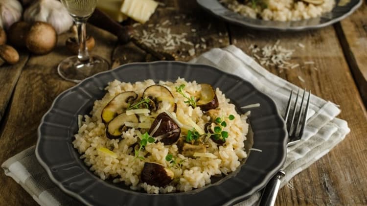Mushroom risotto on a rustic wooden table with white wine in a glass